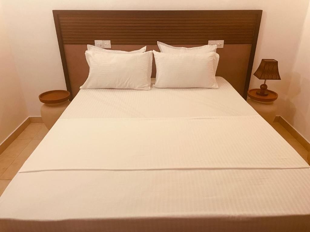Una cama bien hecha con tablero de madera, dos almohadas, una mesita de noche con una lámpara y una pequeña bandeja.