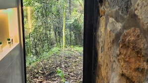 Un baño con vista a un área boscosa a través de una puerta de cristal.