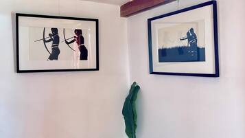 Une pièce avec deux tableaux encadrés accrochés au mur, une petite table sur laquelle est posée une plante, et des poutres en bois apparentes au plafond.