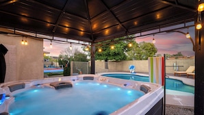 Un jacuzzi con un patio cubierto, una piscina y sillas de descanso.