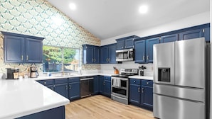 Una cocina moderna con armarios azul marino, electrodomésticos de acero inoxidable y un salpicadero con estampado.