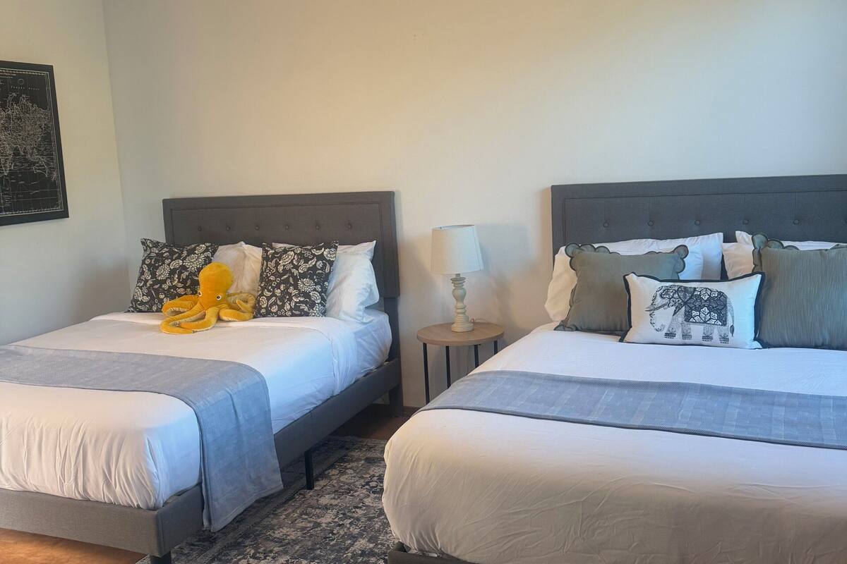 Two single beds with headboards, a ceiling fan, a nightstand with a lamp, and a patterned rug.
