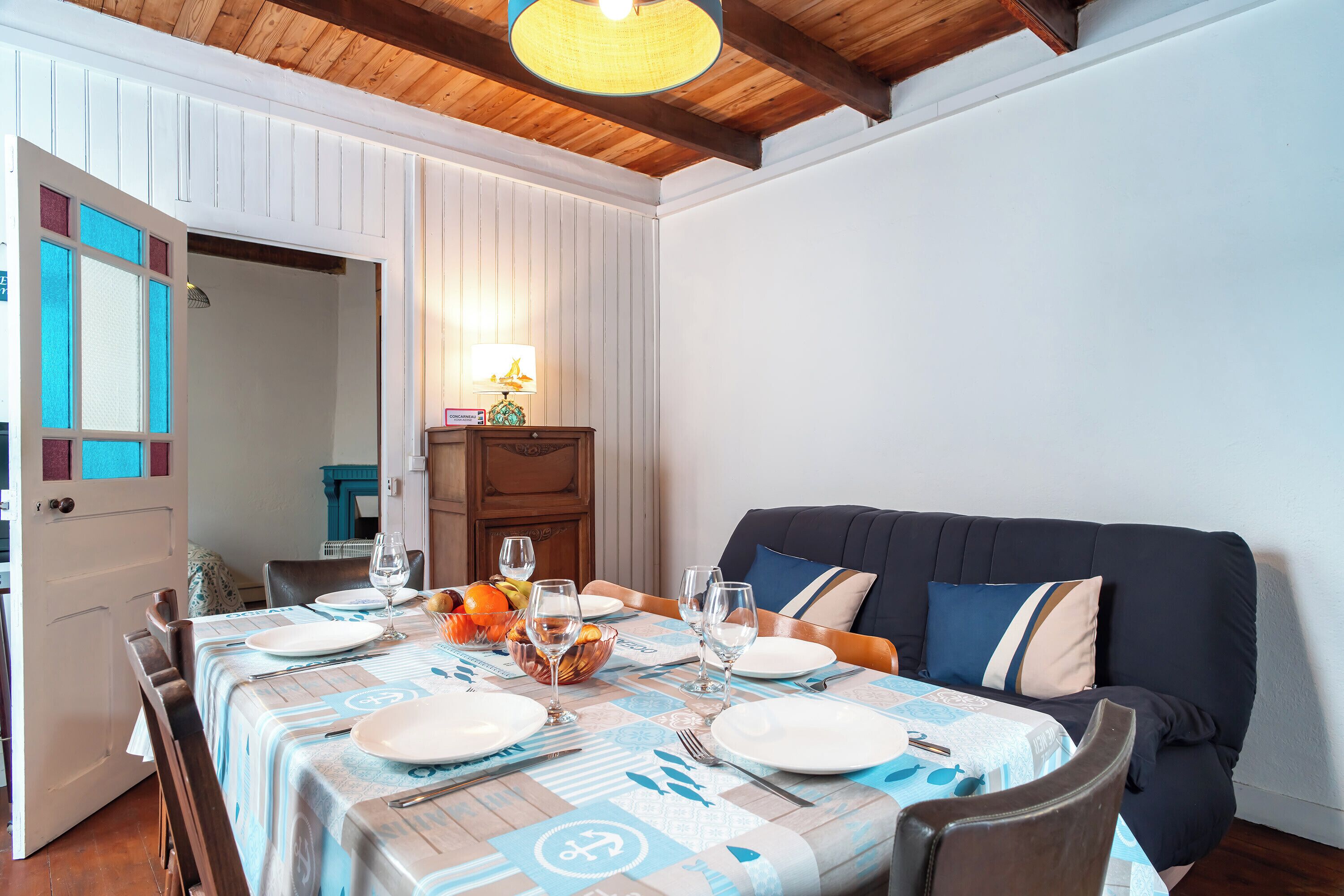 A dining area with a table set for four, a sofa, and a wooden ceiling.
