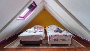 Ein schrägwangiges Schlafzimmer im Dachgeschoss mit zwei Betten, einem Oberlicht und einem gemusterten Teppich.