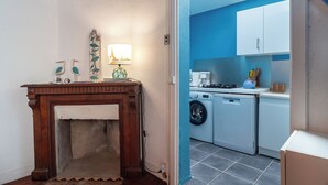 Ein Zimmer mit Kamin, einem kleinen Tisch mit Dekoration und einer Küchenzeile mit Geräten.