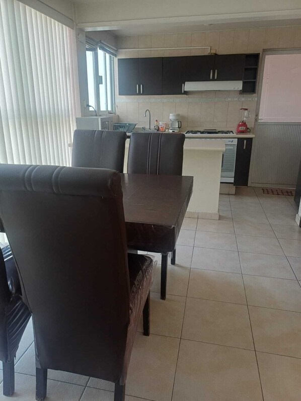 Una cocina moderna con armarios oscuros, una isla central y un comedor con sillas oscuras.