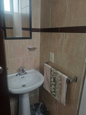 Un baño con lavamanos blanco, un espejo, toallero con toalla y un cubo de basura.