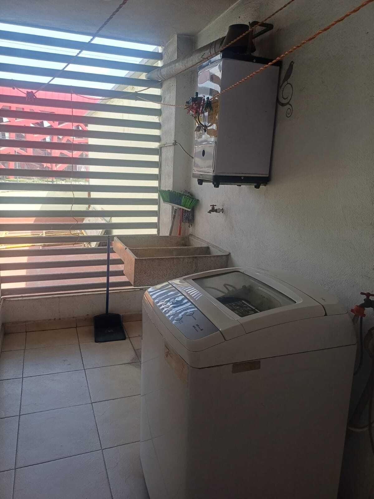 Un área de lavandería con lavadora, un tendedero y una ventana con persianas.