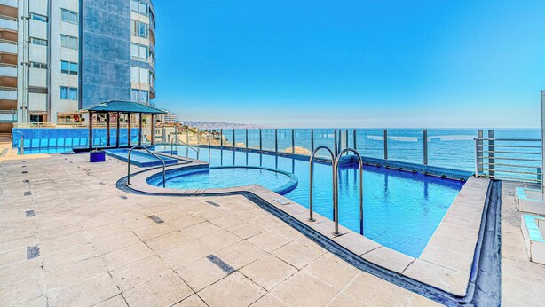 A rooftop pool with a view of the sea, a covered seating area, and a building with multiple balconies. - Vista Pacífico- 2D , Sea View and Wifi (Viña del Mar)