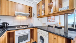 A compact kitchen with wooden cabinets, a built-in oven, a washing machine, and a coffee maker. - Vista Pacífico- 2D , Sea View and Wifi (Viña del Mar)