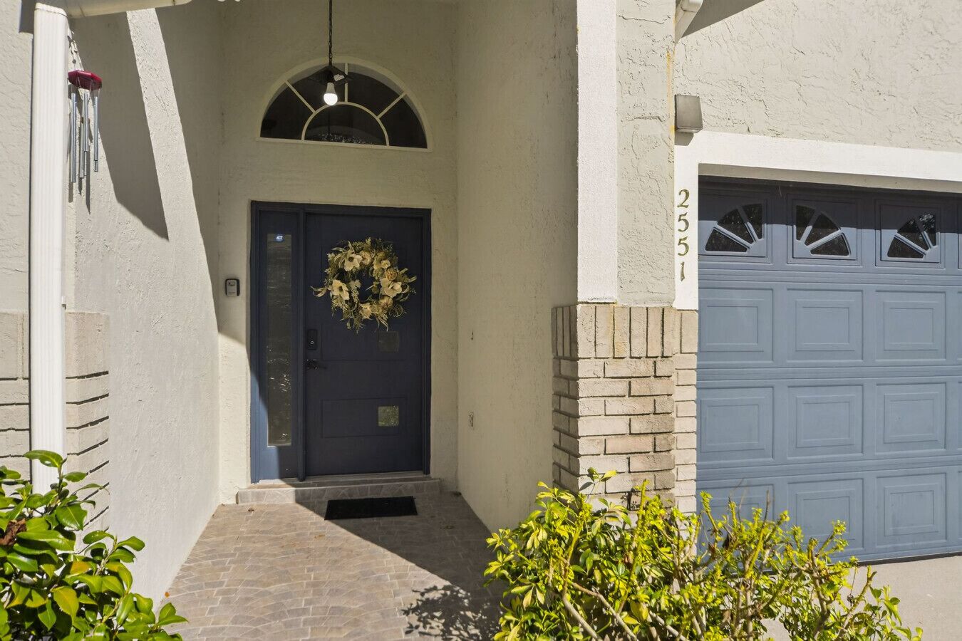 Une maison avec une porte d’entrée bleu foncé, une guirlande décorative, une porte de garage et un pilier en briques.
