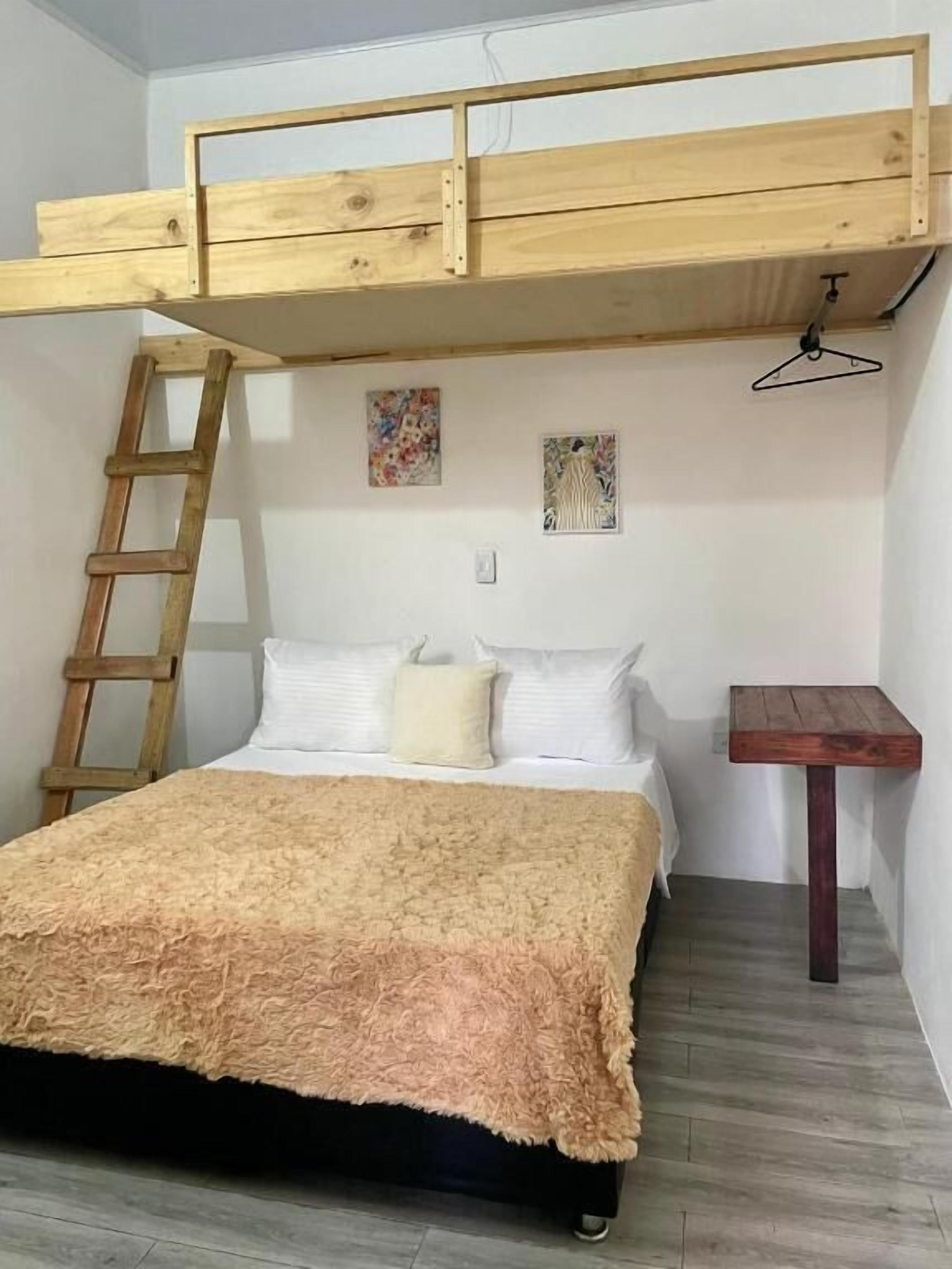 A bunk bed with a wooden ladder, a small table, and two wall art pieces.