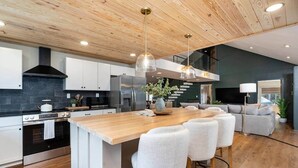 Une cuisine moderne dotée d’un îlot central, d’appareils électroménagers en acier inoxydable et d’un plafond en bois.