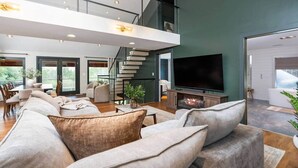 Un salon moderne doté d’un grand téléviseur, de sièges confortables, d’une cheminée et d’un escalier menant à un niveau supérieur.