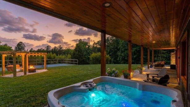 Un bain à remous avec une terrasse en bois, une pergola illuminée de guirlandes lumineuses et une pelouse verdoyante.