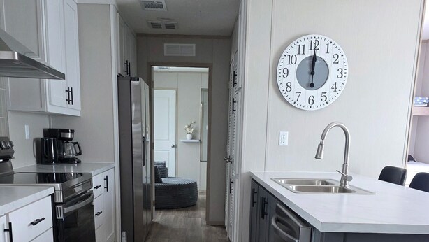 A modern kitchen with white cabinets, a stainless steel range, a built-in oven, a coffee maker, a sink, and a large wall clock. - Welcome to vacation Home five minutes from the beach. 🏖️ (Pensacola)