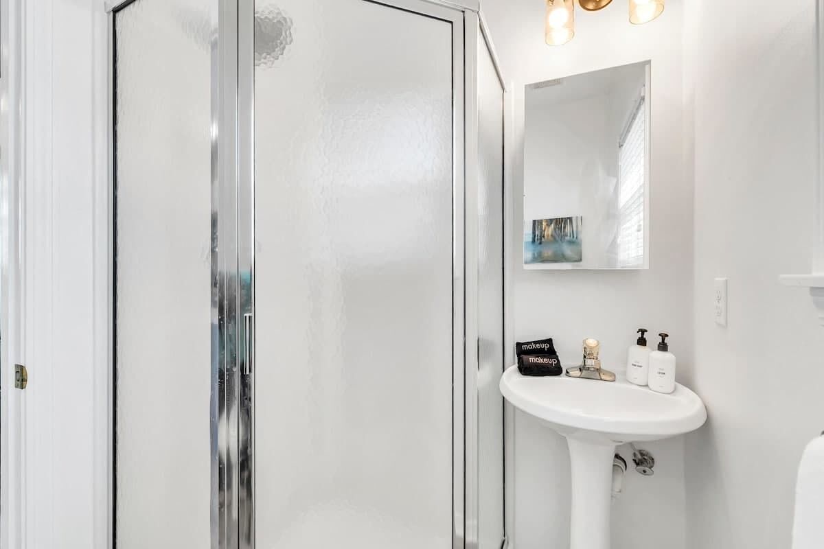 Un baño con mampara de vidrio, lavamanos blanco y espejo sobre él.