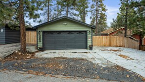 A green garage with a black door, surrounded by trees and a wooden fence. - The Hideaway (Big Bear Lake)