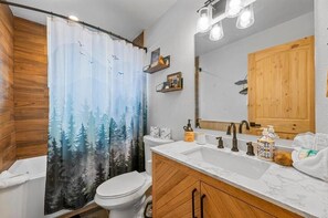 Un baño con cortina de ducha con motivos de bosque, un inodoro, un lavabo con espejo y armarios de madera.