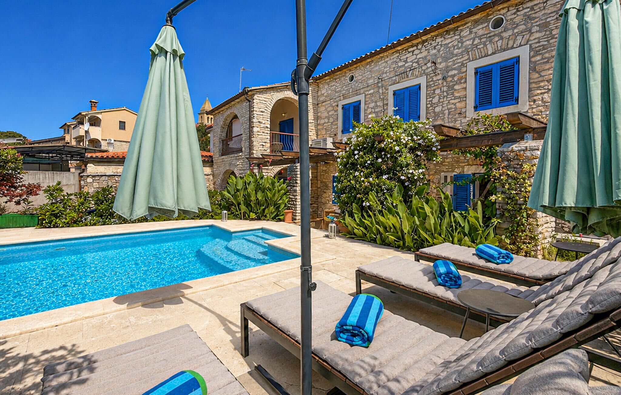 A poolside area with lounge chairs, a pool, and stone buildings with blue shutters.