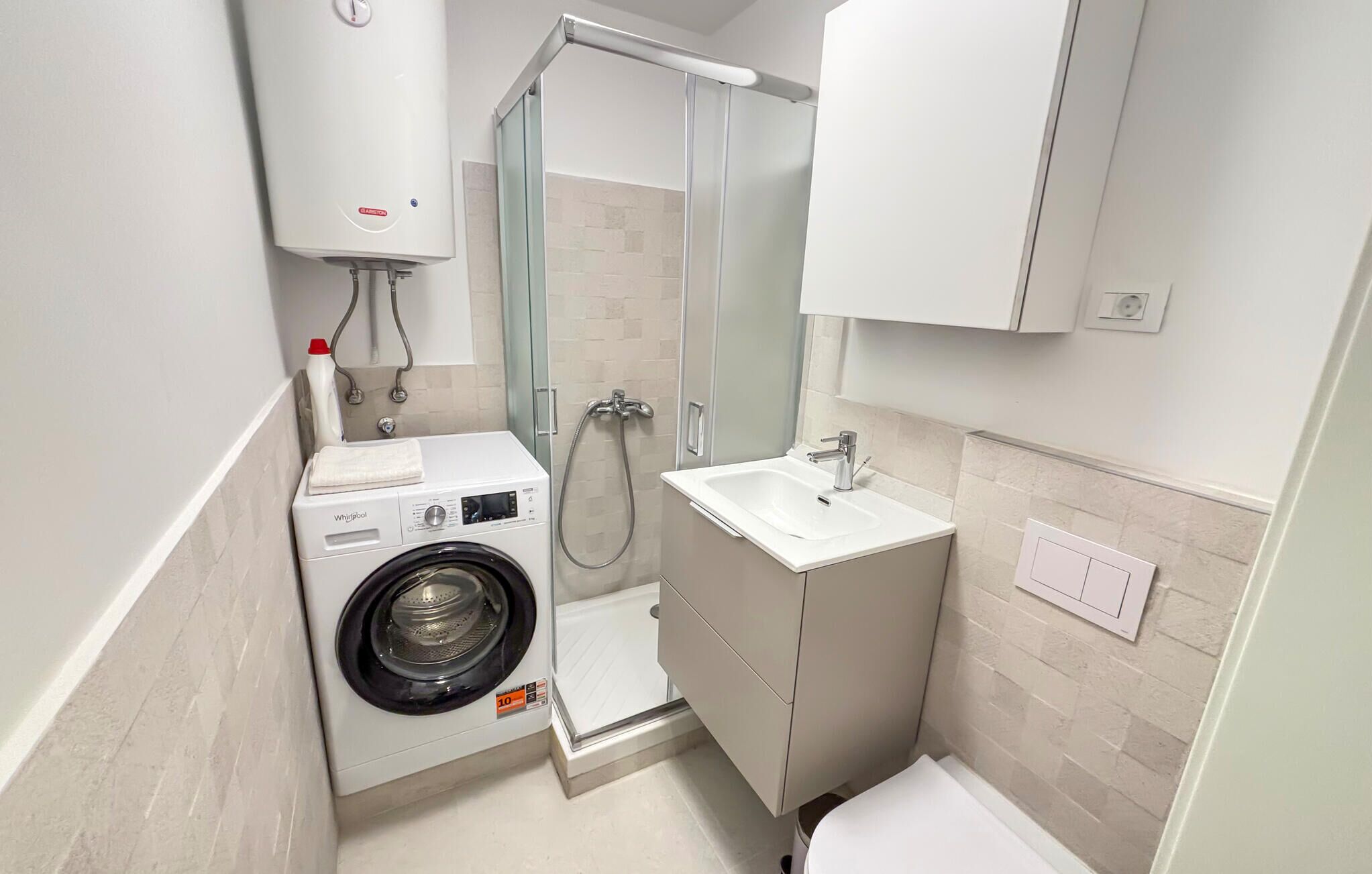 Une salle de bain compacte équipée d’un lave-linge intégré, d’une cabine de douche et d’un lavabo.