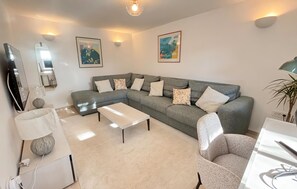 Ein Wohnzimmer mit grauem Sofa, einem weißen Couchtisch, einem grauen Sessel und einer Lampe.