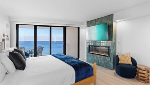 Een slaapkamer met een bed, een televisie, een open haard, uitzicht op zee en een balkon.