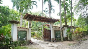 A gated entrance with a pergola, surrounded by lush greenery and palm trees.