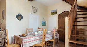 A dining area with a table set for four, wooden chairs, a wooden staircase, and a large wooden cabinet. - Gîtes de France® - Graine de Lin (AMBRUMESNIL)
