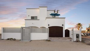 Una casa moderna de dos pisos con entrada protegida por un portón, un patio cubierto y un garaje.