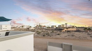 Paisaje desértico con edificios, cielo despejado y un atardecer.