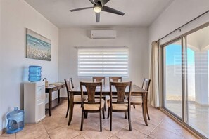 Comedor con mesa, sillas, ventilador de techo, ventana con persianas y dispensador de agua.