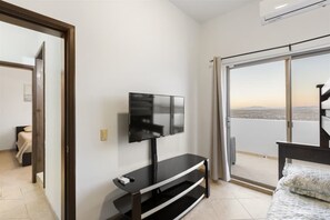 A room with a TV on a stand, a bed, and a balcony with a view.