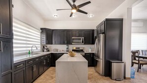 Una cocina moderna con armarios oscuros, una isla central, electrodomésticos de acero inoxidable y un ventilador de techo.