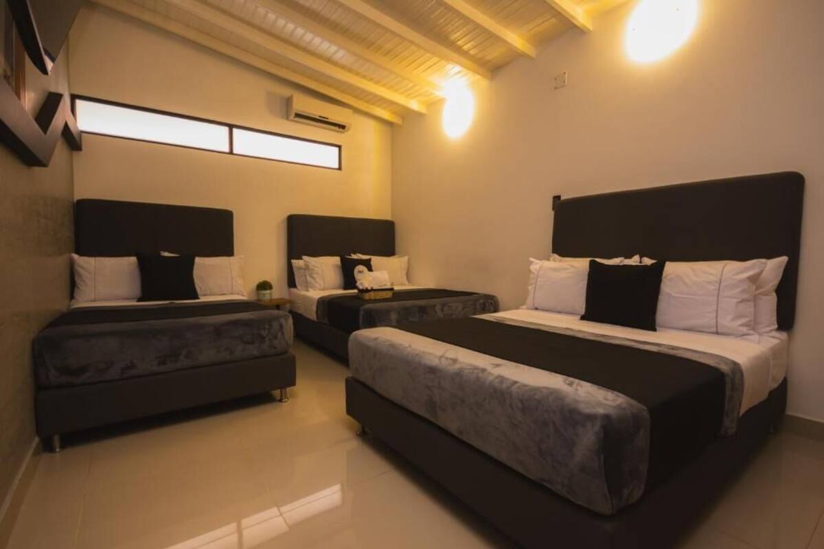 Quarto de hotel com três camas, uma televisão de tela plana e uma luminária no teto.