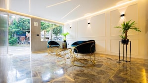 A modern lobby with marble flooring, two blue velvet armchairs, a black floor lamp, and a potted plant. - Boutique N Laureles (Medellín)