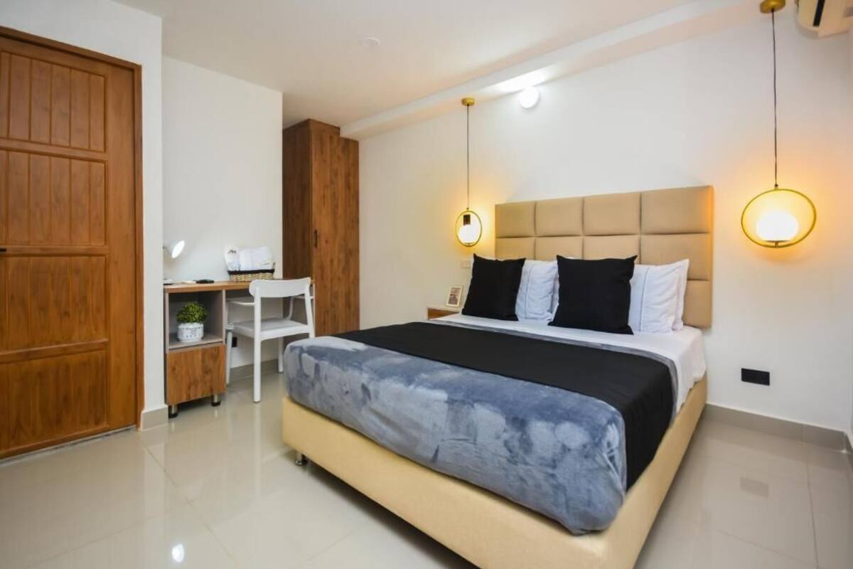 Quarto moderno com cama grande, guarda-roupa de madeira, escrivaninha e luminária pendente.