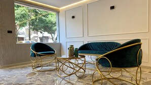 A room with a marble floor, a green sofa, two blue chairs, and a small table with a vase. - Boutique N Laureles (Medellín)