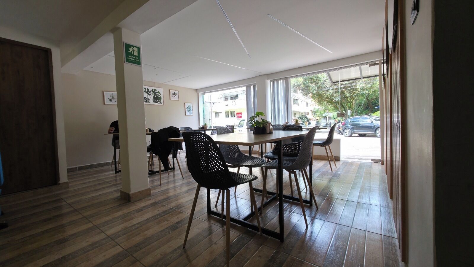 A dining area with a wooden floor, a table with chairs, and a view of the street outside.