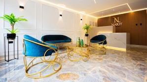 A reception area with a wooden reception desk, blue upholstered chairs, a marble floor, and wall-mounted lighting. - Boutique N Laureles (Medellín)