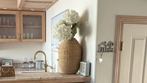 Una cucina con mobili in legno, uno sgabello da bar, un cesto di vimini e un vaso con fiori.