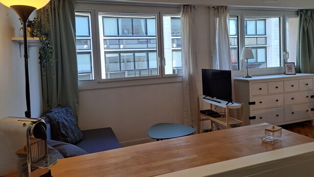 Una habitación con una mesa de madera, un televisor sobre un mueble, un sofá, una mesita redonda y un aparador blanco.