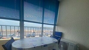 Ein Zimmer mit Tisch, Stühlen, einem Fenster mit Jalousien, einem Heizkörper und Blick auf einen Parkplatz.