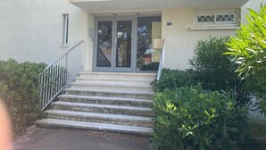 Ein zweistöckiges Gebäude mit Hauseingang, einem Balkon im oberen Stockwerk und einer Treppe aus Beton, die zur Tür hinaufführt.
