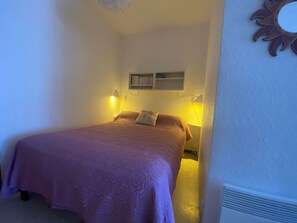 A bedroom with a bed, bedside lamps, a shelf with books, and a decorative sun on the wall. - Apartment, pets welcome, AC - lake view (Balaruc-les-Bains)