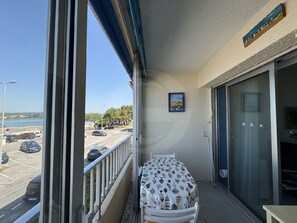 A balcony with a table and chairs, a view of a parking lot and beach, and a framed picture on the wall. - Apartment, pets welcome, AC - lake view (Balaruc-les-Bains)