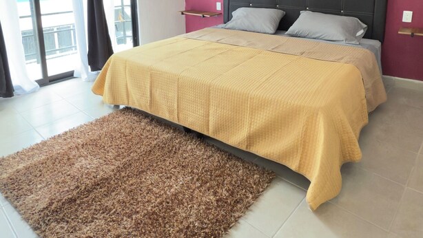 Un dormitori amb un llit, una catifa, una finestra amb cortines i una paret rosa.