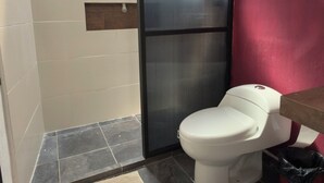 Un bany petit amb vàter, plat de dutxa i una paret vermella decorativa.