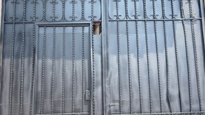 Una reixa de metall amb barres verticals i una secció rectangular central, una petita llum penjant a dalt i un teulat amb un disseny decoratiu.