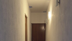 Passadís estret amb rajoles estampades, una porta de fusta i una làmpada a la paret.